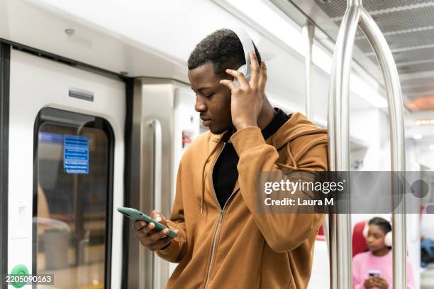 young man listening to music on his phone while commuting by subway train - auscultador equipamento áudio imagens e fotografias de stock