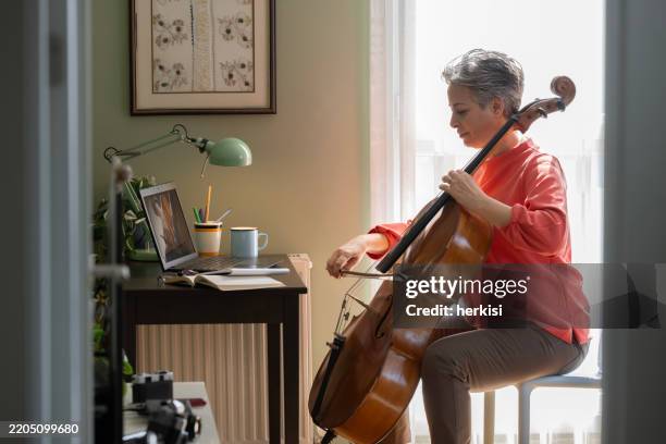 woman watching a tutorial on laptop on how to play cello - play cello stock pictures, royalty-free photos & images