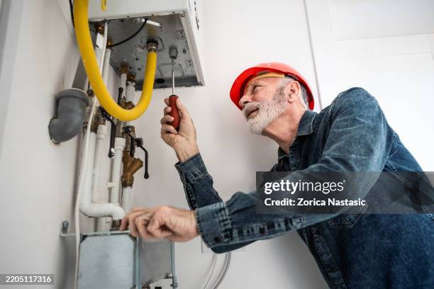 techniker, der das rohrleitungssystem im verteiler-wandschrank einstellt - heizungsmonteur stock-fotos und bilder