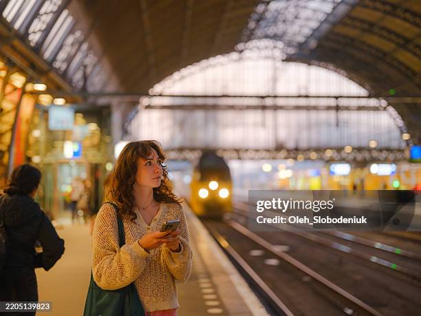mujer usando un teléfono inteligente esperando el tren en ámsterdam - andén de estación de tren fotografías e imágenes de stock