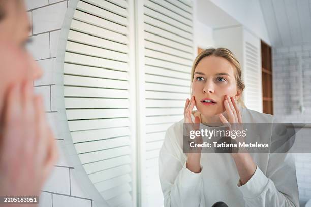 skin analysis in mirror. focused woman examines her face for signs of aging and wrinkles in bathroom - caratteristica della pelle foto e immagini stock