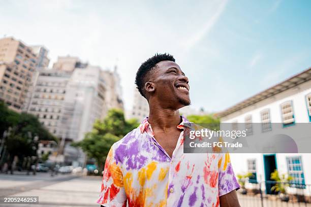 hombre joven caminando y mirando alrededor en la calle - mirar alrededor fotografías e imágenes de stock
