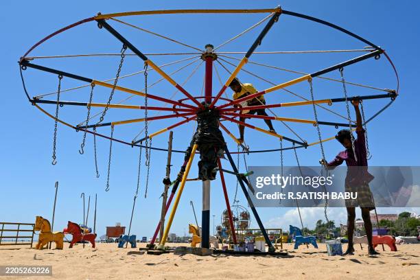 Workers paint a merry-go-round during a hot afternoon, at Marina beach in Chennai on March 19, 2025.