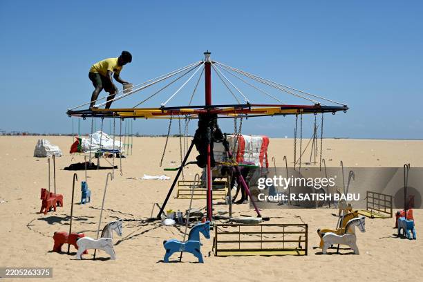 Workers paint a merry-go-round during a hot afternoon, at Marina beach in Chennai on March 19, 2025.