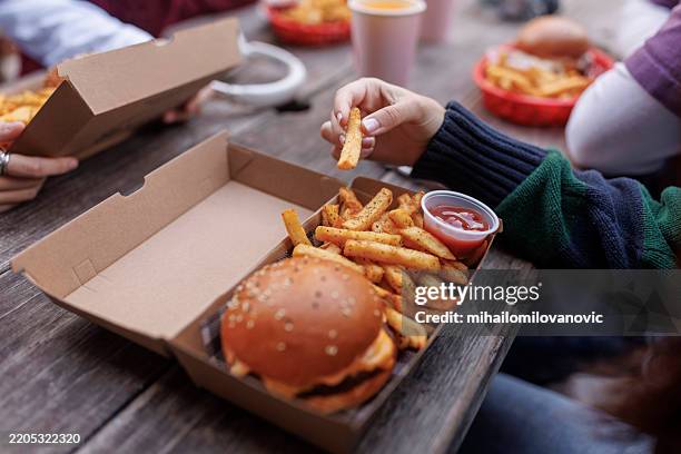 primo piano della mano che tiene i fuochi francesi con l'hamburger - junk food foto e immagini stock