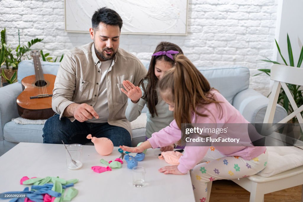 Father Conducts Balloon Experiment With Daughters Inflating Balloons Using Baking Soda