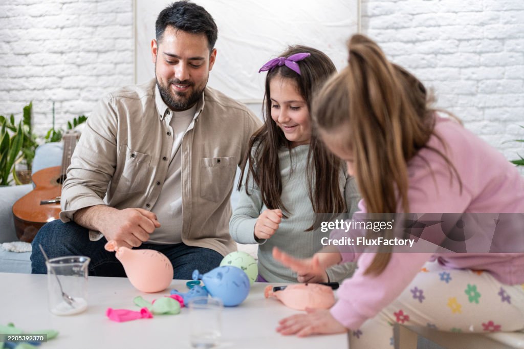 Father engaging in an educational balloon activity with his daughters at home