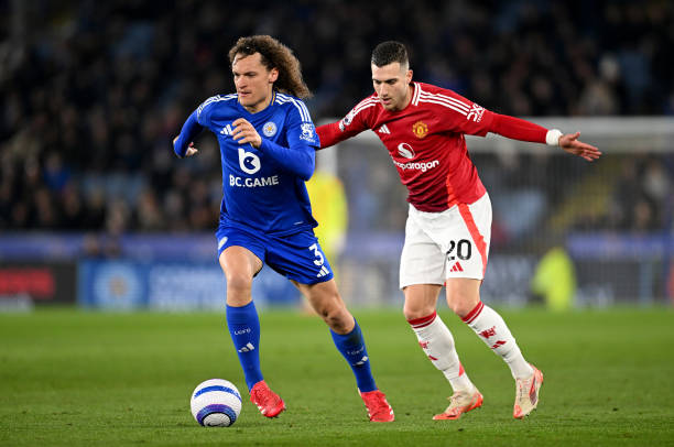 Wout Faes of Leicester City runs with the ball under pressure from Diogo Dalot of Manchester United during the Premier League match between Leicester...