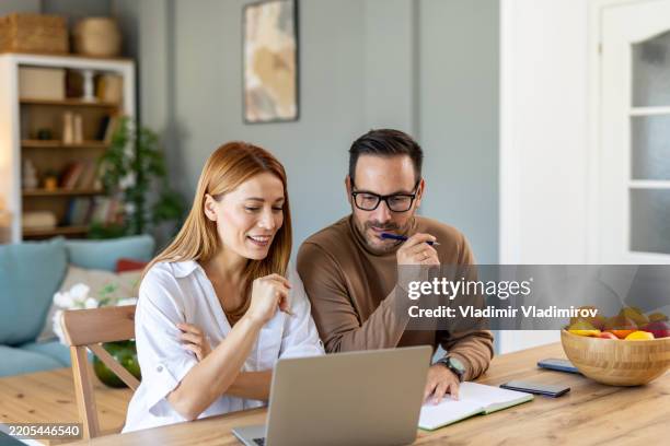 couple travaillant à la maison, utilisant un ordinateur portable et regardant les finances - deux parents photos et images de collection