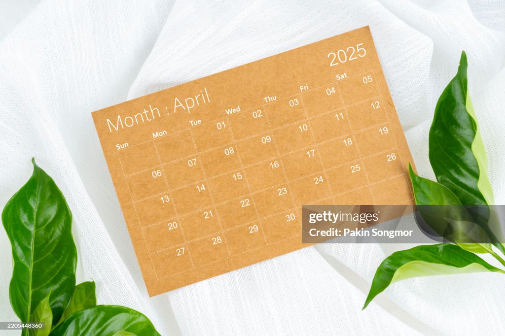 April 2025 brown calendar page with green leaves on white textile.