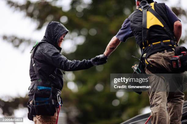 two men passing a tool on a construction site - dakdekker stockfoto's en -beelden