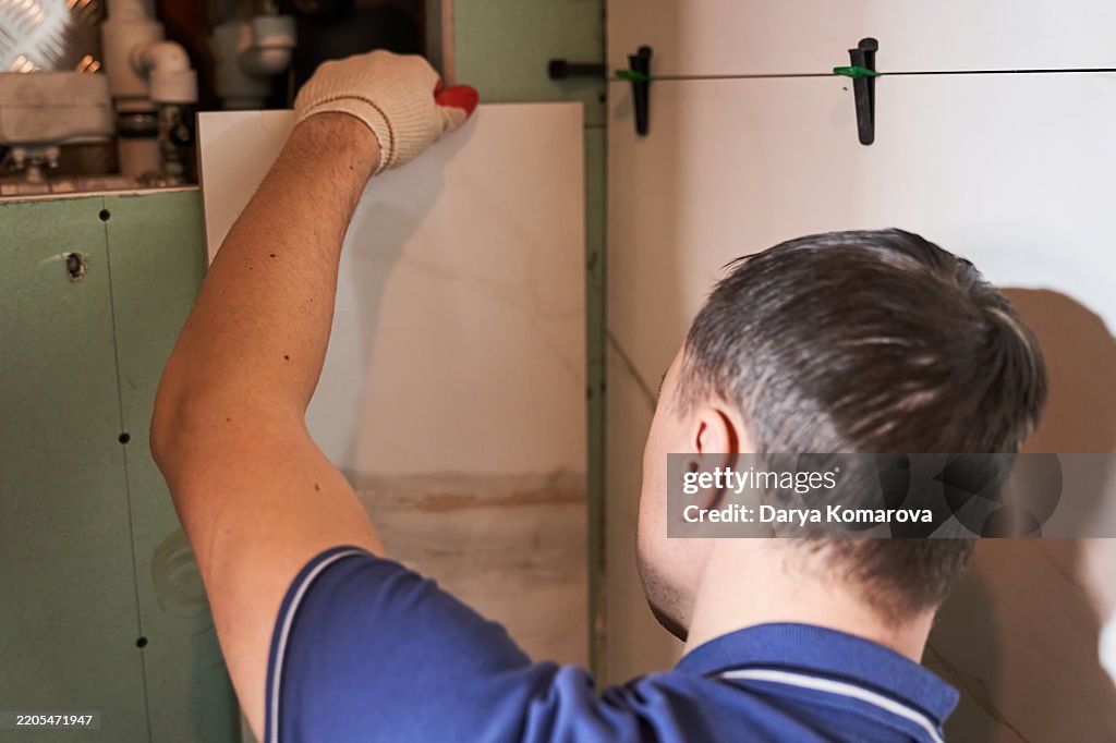 A man tries on a tile on the wall, checks the pattern on the tile. Modern repair with big tile.