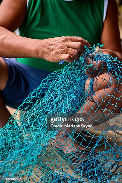 a fisherman carefully stitching a teal-colored nylon fishing net. - nylon imagens e fotografias de stock