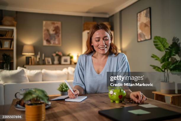 woman managing home finances and savings with piggy bank - welvaart stockfoto's en -beelden