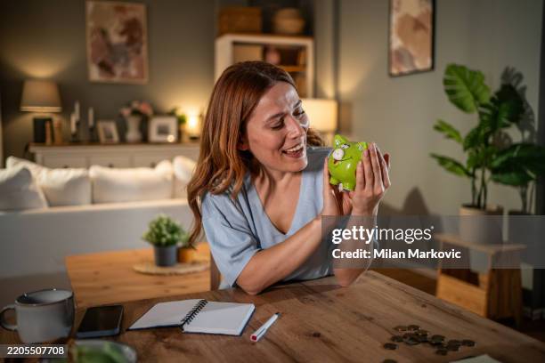 happy woman holding piggy bank at home calculating savings - welvaart stockfoto's en -beelden