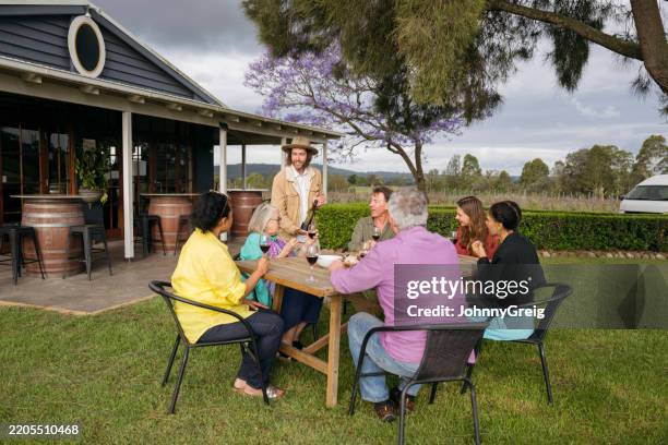 smiling event host presenting red selection to wine tasters - pokolbin stock pictures, royalty-free photos & images