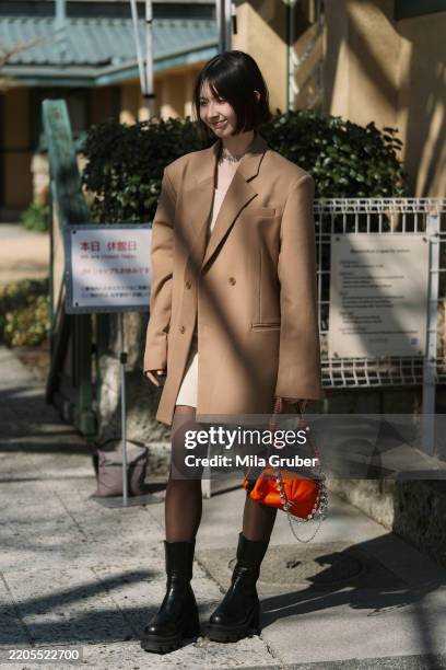 Guest is seen wearing a beige oversized jacket, mini dress, orange Topologie & Maison Kitsune bag and black boots during Rakuten Tokyo Fashion Week...