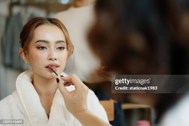 beautiful bride prepares for her wedding with professional makeup artist and hairstylist. - bridal make up stock pictures, royalty-free photos & images
