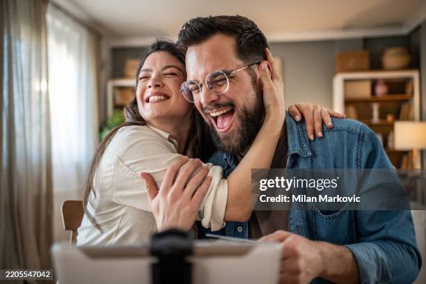 happy couple embracing while making a video call at home - boa notícia imagens e fotografias de stock