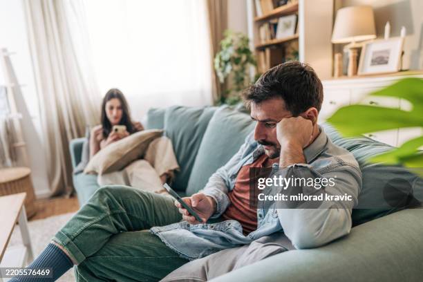 pareja que experimenta problemas de comunicación mientras usa teléfonos inteligentes en el sofá - distante fotografías e imágenes de stock