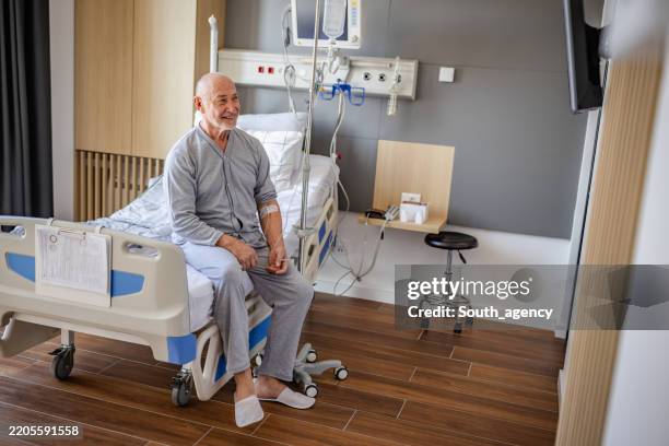 senior man sits on hospital bed during recovery in a well-equipped medical room - ill equipped stock pictures, royalty-free photos & images