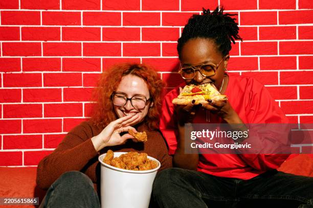 two friends laughing and enjoying fast food - gefrituurde kip stockfoto's en -beelden