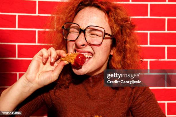 redhead woman enjoying spicy fried chicken - specerij stockfoto's en -beelden