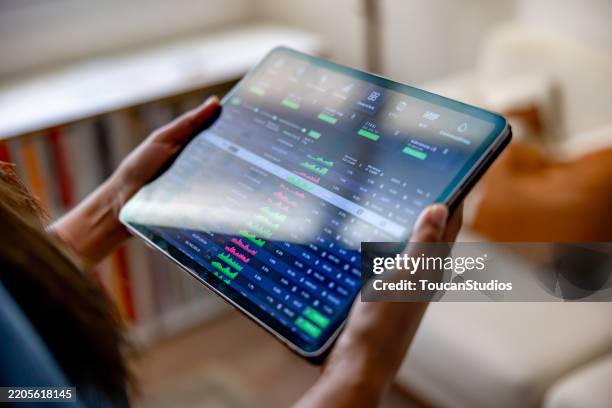 woman at home investing in the stock market using an app on her tablet - voorspellen stockfoto's en -beelden