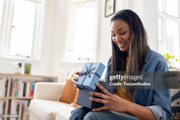 frau lächelt beim öffnen eines geburtstagsgeschenks zu hause - geburtstagsgeschenk stock-fotos und bilder