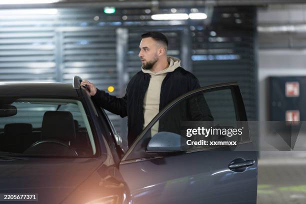 a young caucasian man getting in his car in an underground garage - car door stock pictures, royalty-free photos & images