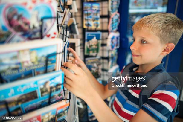 little boy selecting postcards at a display stand in a small italian town - souvenir stock pictures, royalty-free photos & images