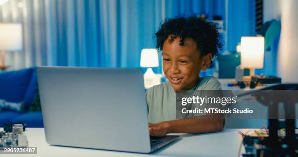 young african-american boy learning programming codes on laptop, engaged in stem learning project involving robotics in home at night. stem education robotics courses online. - computer coding game stock pictures, royalty-free photos & images