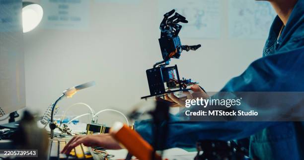 closeup young female engineer working late on robotic arm prototype in tech lab at night. machine learning, computer manufacturing, innovation and creativity. ai and robotics development. - invento fotografías e imágenes de stock