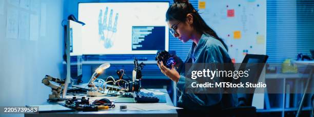 joven ingeniera trabajando hasta tarde en un prototipo de brazo robótico en un laboratorio tecnológico por la noche. machine learning, fabricación asistida por ordenador, innovación y creatividad. desarrollo de ia y robótica. - robótica fotografías e imágenes de stock