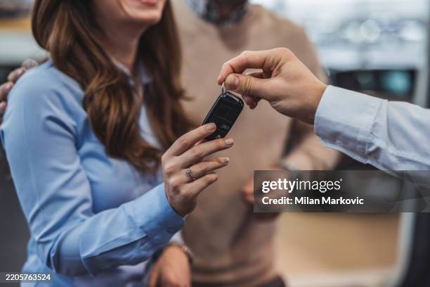 happy couple receiving new car keys from salesman in dealership - car key stock pictures, royalty-free photos & images