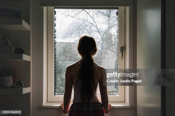 rear view of a teenage girl looking out of her bedroom window on a sunny day - negative emotion - alleen één tienermeisje stockfoto's en -beelden