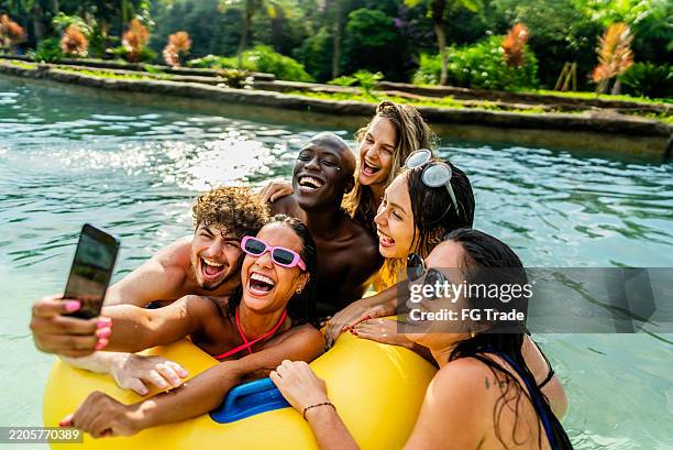 friends taking selfies on the mobile phone on a swimming float in a swimming pool at a water park - vriendschap stockfoto's en -beelden