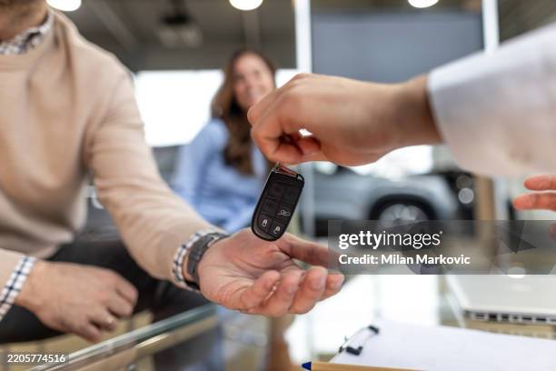 car salesman giving keys to a new car owner in a dealership - autokredit stock-fotos und bilder