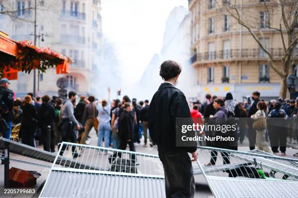 Man stands in front of a barricade and watches demonstrators march past during a protest against the far right, racism, and anti-Semitism, in Paris,...