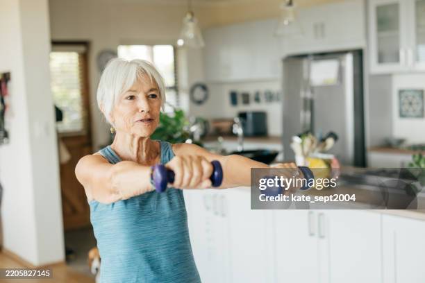 home fitness routine for older adults: senior woman lifting small dumbbells in a bright living room. - vorbeugung stock-fotos und bilder