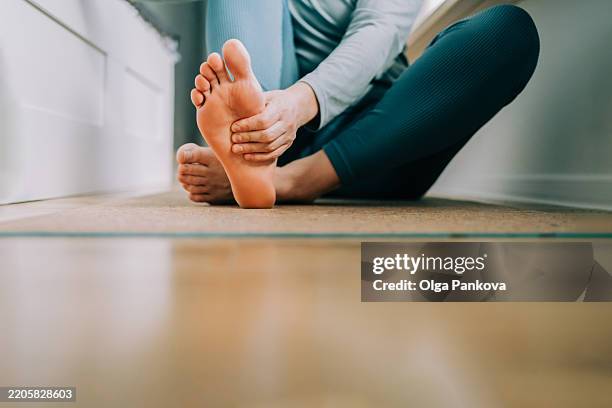 woman massages her feet on yoga mat - pie humano fotografías e imágenes de stock