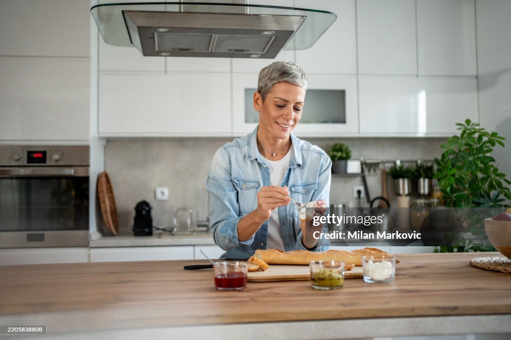 Smiling woman spreading cream cheese on bread in modern kitchen