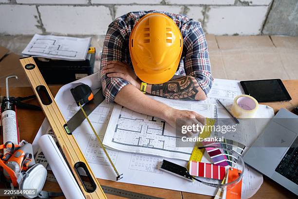 tired construction worker sleeping over blueprints at work desk - construction mistake stock pictures, royalty-free photos & images