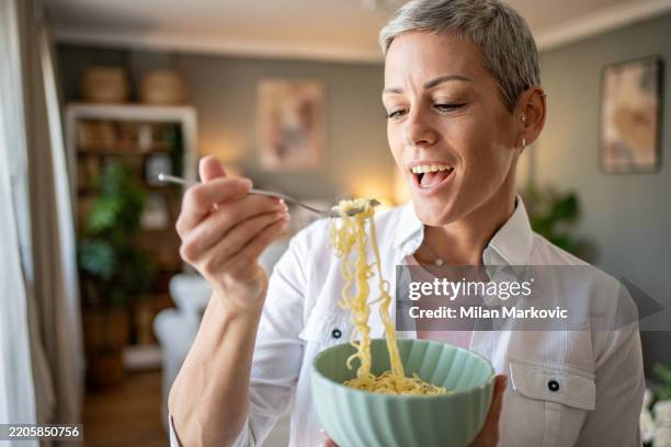 mujer feliz comiendo fideos con tenedor en casa - carbohidrato fotografías e imágenes de stock