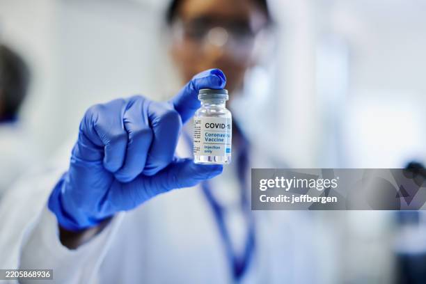 a shot of a doctor holding up a vial of a covid-19 vaccine - covid 19 vaccine stock pictures, royalty-free photos & images