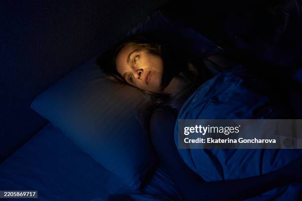 woman lying awake in bed late at night with dim lighting - insomnia stock-fotos und bilder
