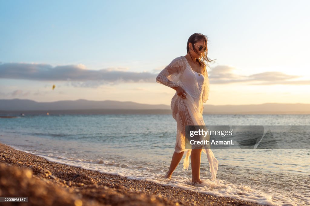 Reife Asiatische Frau In Weißem Spitzenkleid, Die Während Der Goldenen Stunde Barfuß Am Strand Läuft