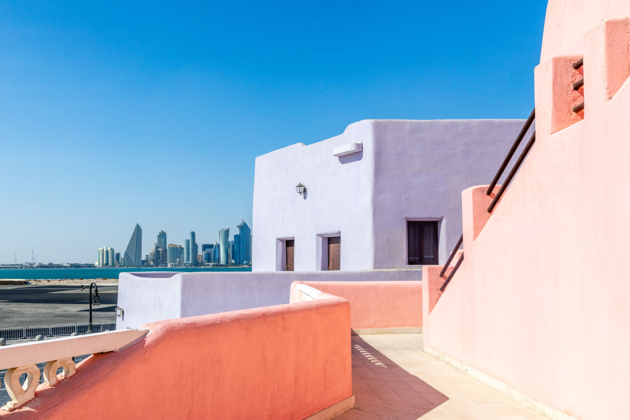 Colorful Mina village district street with arab traditional shaped buildings and modern downtown in the background, Doha, Qatar Colorful Mina village district street with arab traditional shaped buildings and modern downtown in the background, Doha, Qatar