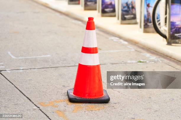 bright orange and white traffic cone standing on sidewalk - cone de trânsito imagens e fotografias de stock