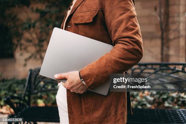 professional individual holding a laptop in outdoor setting with natural surroundings - under the arm stock pictures, royalty-free photos & images